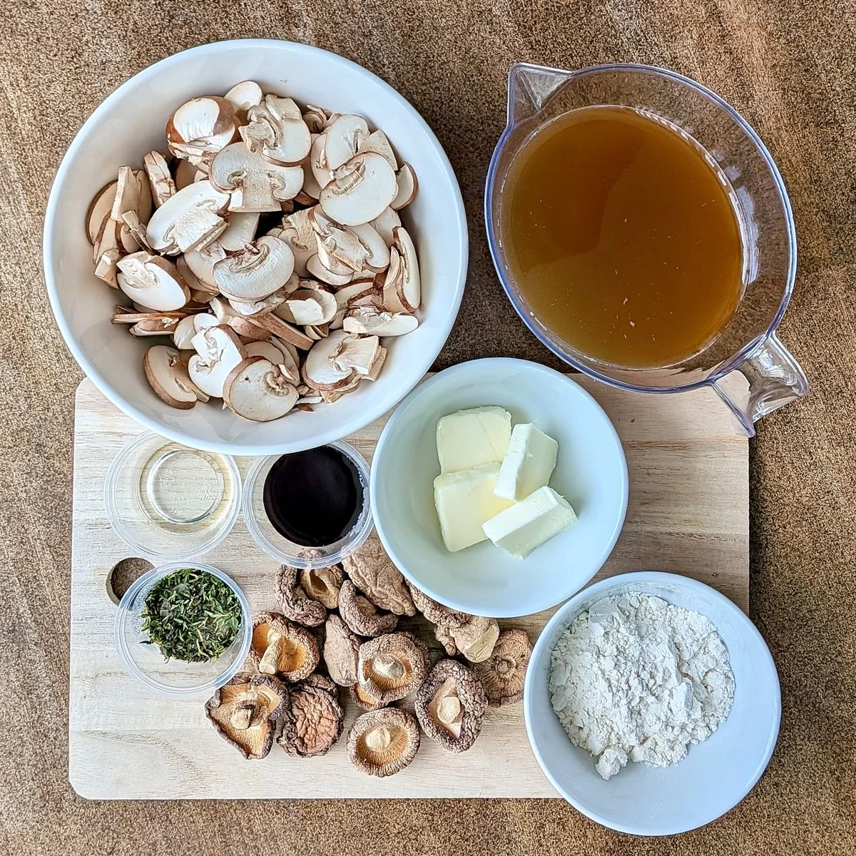 Ingredients for vegetarian mushroom gravy including dried shiitake mushrooms, cremini mushrooms, vegetable broth, butter, flour, soy sauce, thyme, and apple cider vinegar