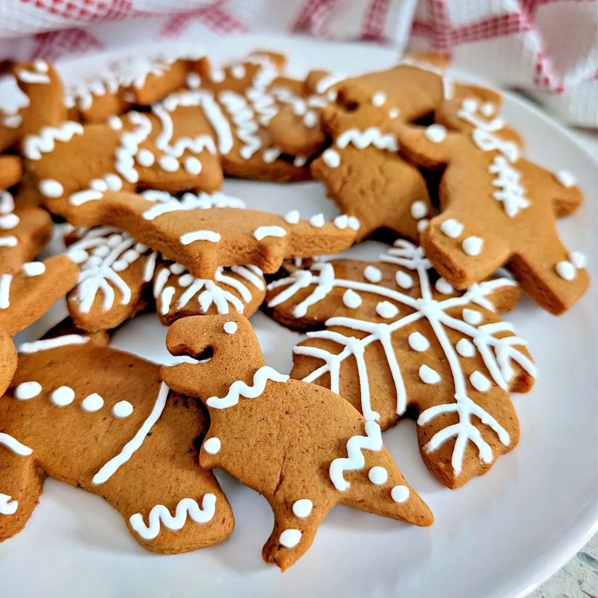 Decorated dinosaur gingerbread cookie with white royal icing on a plate with other gingerbread cookies
