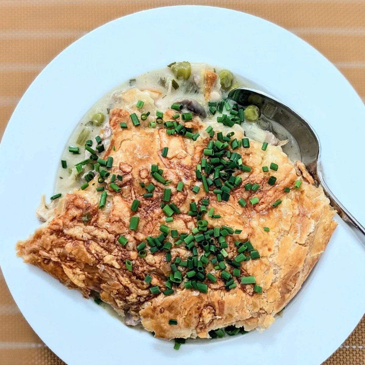 Rotisserie chicken pot pie with puff pastry crust topped with chives in a bowl