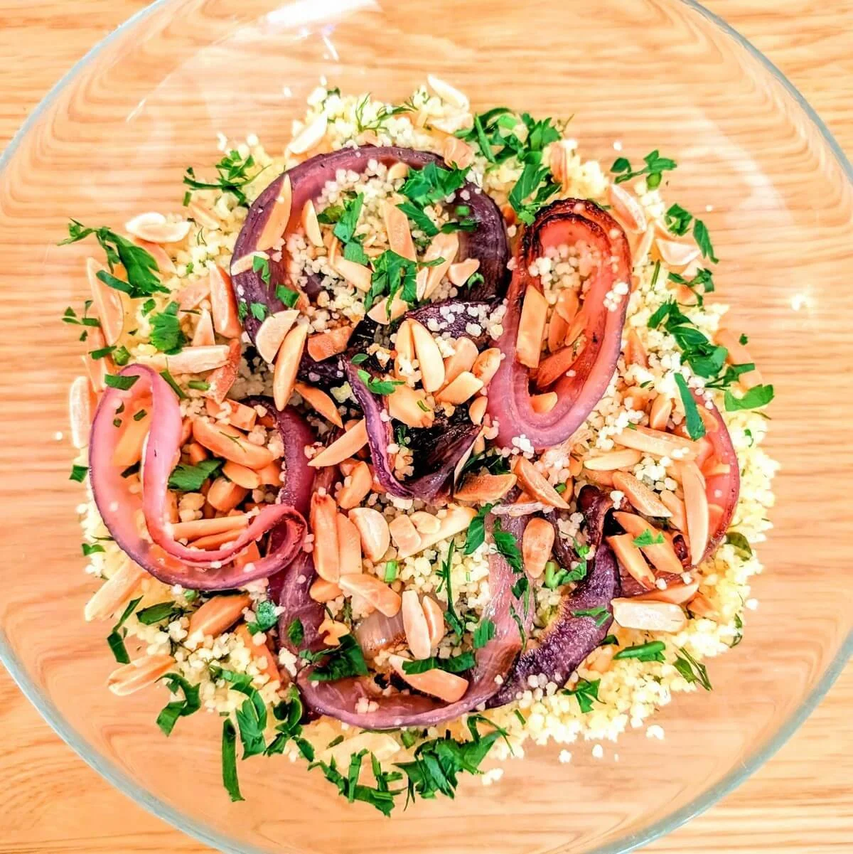 Bowl full of fluffy couscous cooked with electric kettle topped with toasted almonds, onions, herbs, and preserved lemon vinaigrette