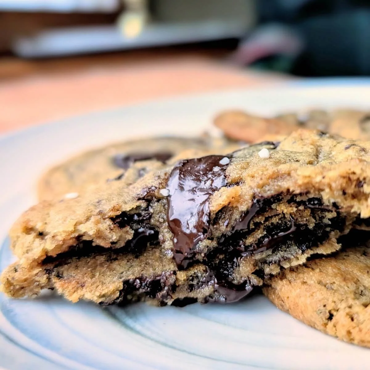 Chewy salted dark chocolate chip cookie broken in half on a plate, with gooey melted chocolate and flaky sea salt
