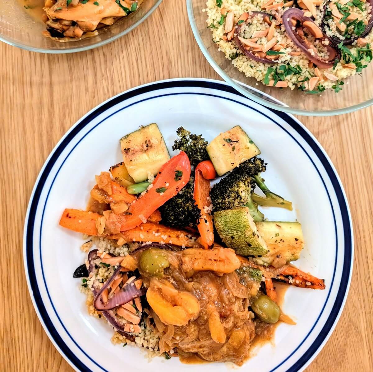 Chicken tagine with couscous and roasted vegetables served on a plate with more preserved lemon chicken tagine in a bowl on the side