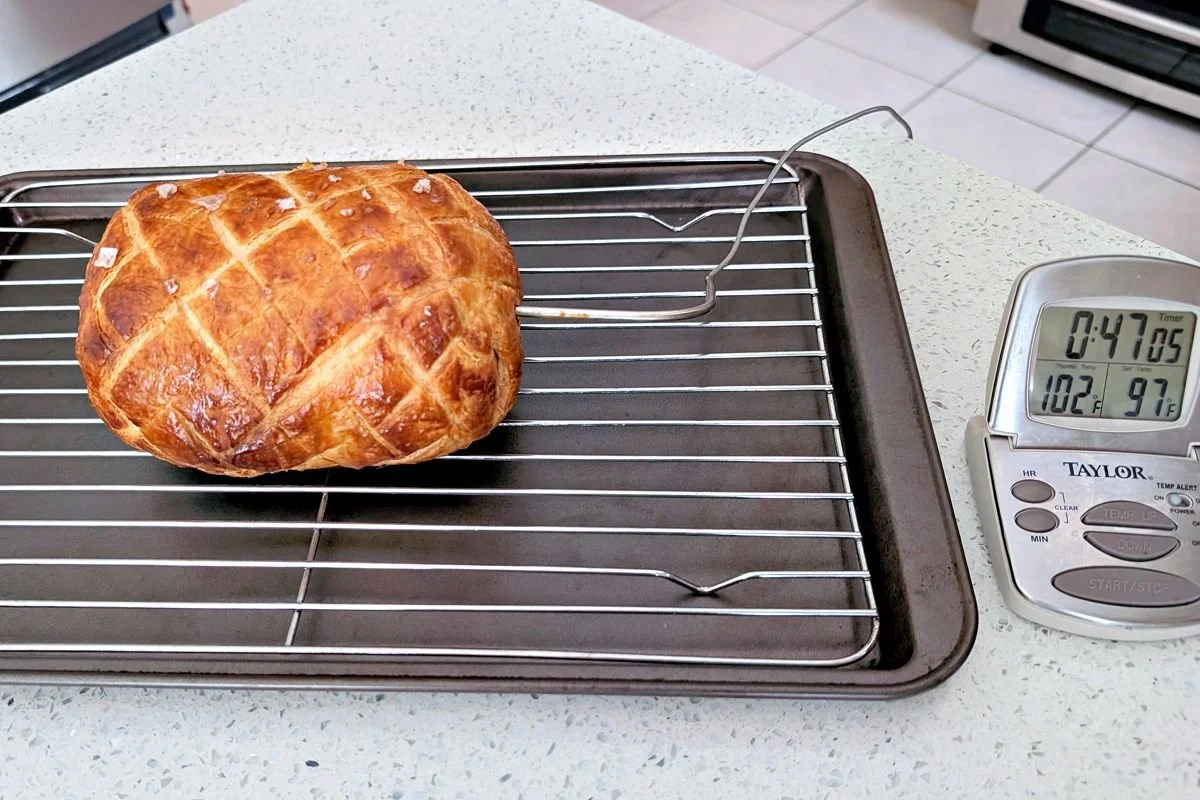 Beef Wellington resting on a wire rack with a probe thermometer monitoring carryover cooking