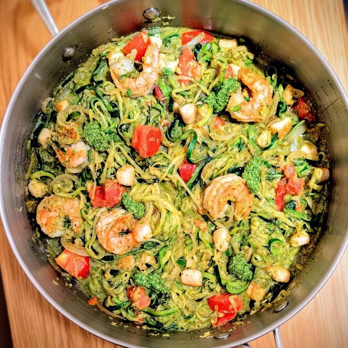 Arugula basil walnut pesto tossed with zucchini noodles shrimp scallops and cherry tomatoes in skillet