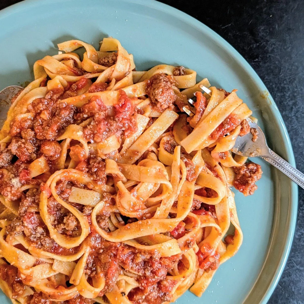 All beef bolognese sauce without pork or dairy served over tagliatelle pasta on a plate with a fork on the side