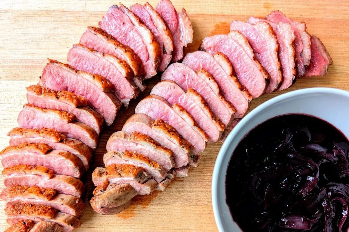 Sliced duck breast with red wine pan sauce arranged on wooden cutting board