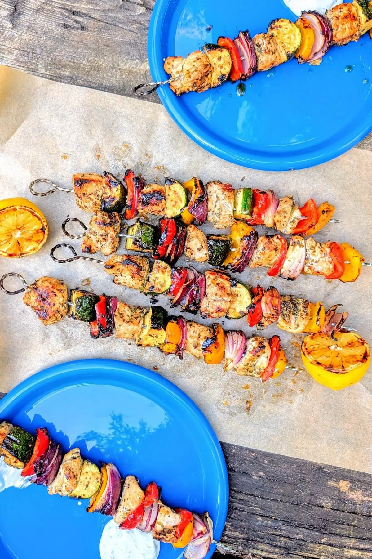 Greek chicken skewers served on parchment paper on a camping table with charred limes and blue plates