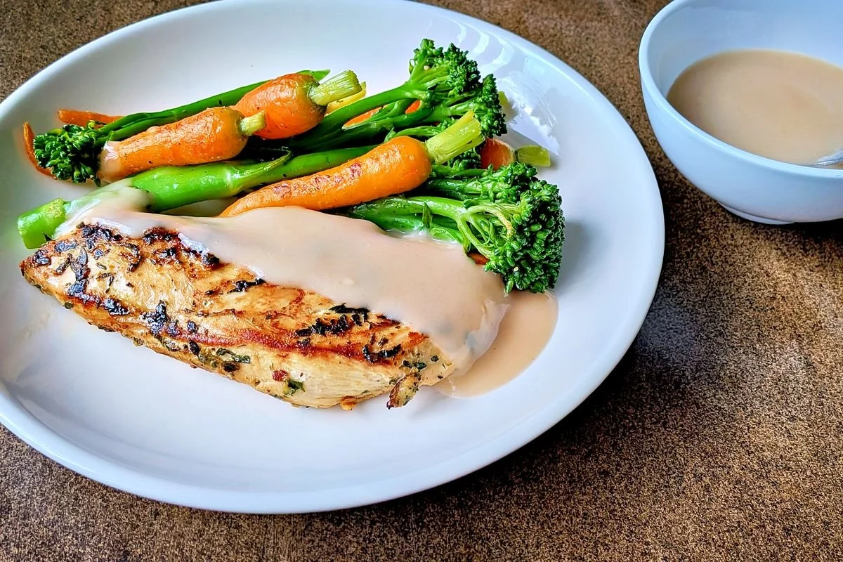 Seared chicken breast with velouté sauce served alongside broccolini and carrots