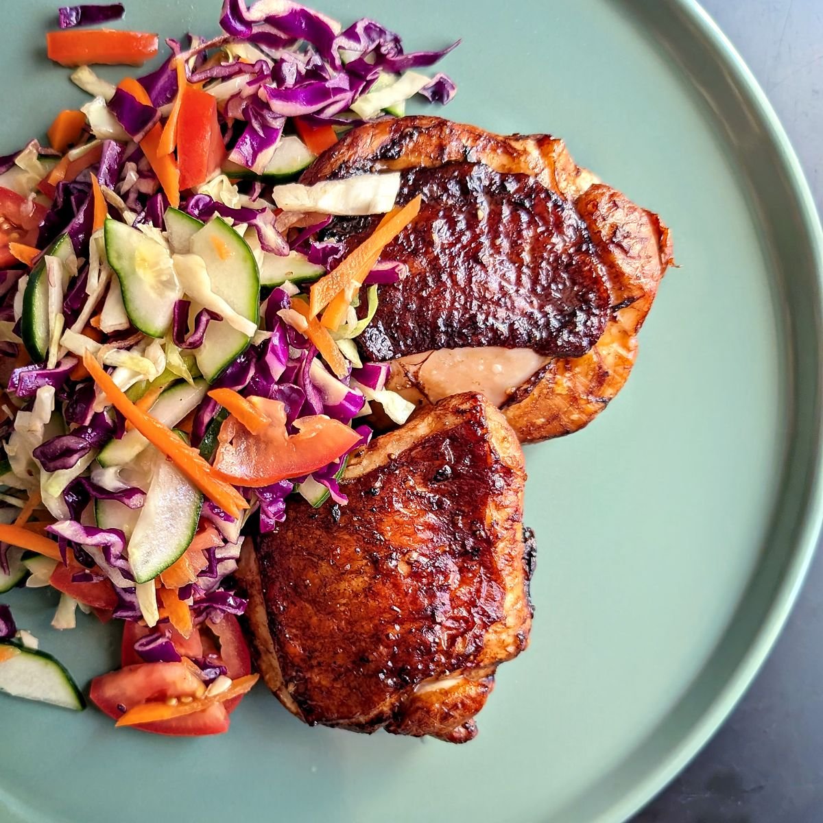 Balsamic chicken thighs cooked in the air fryer served alongside fresh cabbage slaw on a plate