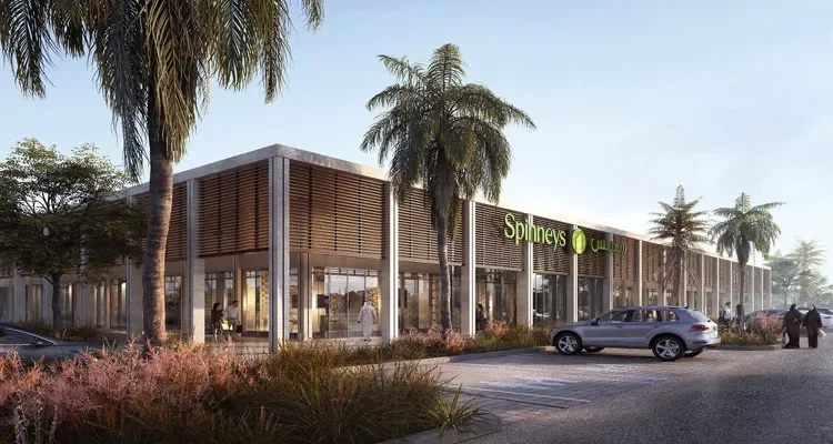 Rendering of a modern shopping mall facade with the name 'Spinneys' in green, surrounded by trees, parked cars, and pedestrians.