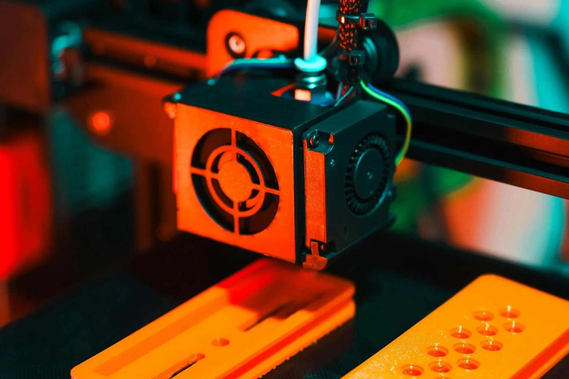Impression d'une imprimante 3D en action avec extrudeuse chauffée. L’image montre la tête d’impression en cours avec une belle lumière colorée, principalement en orange et vert.