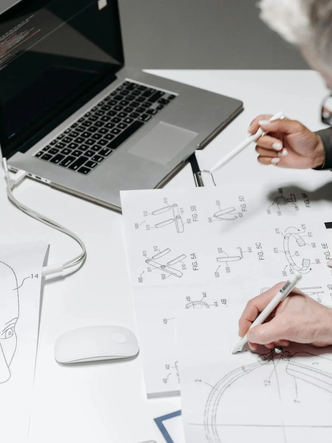 Deux personnes travaillent sur un plan technique ou un schéma à côté d'un ordinateur portable sur une table blanche.