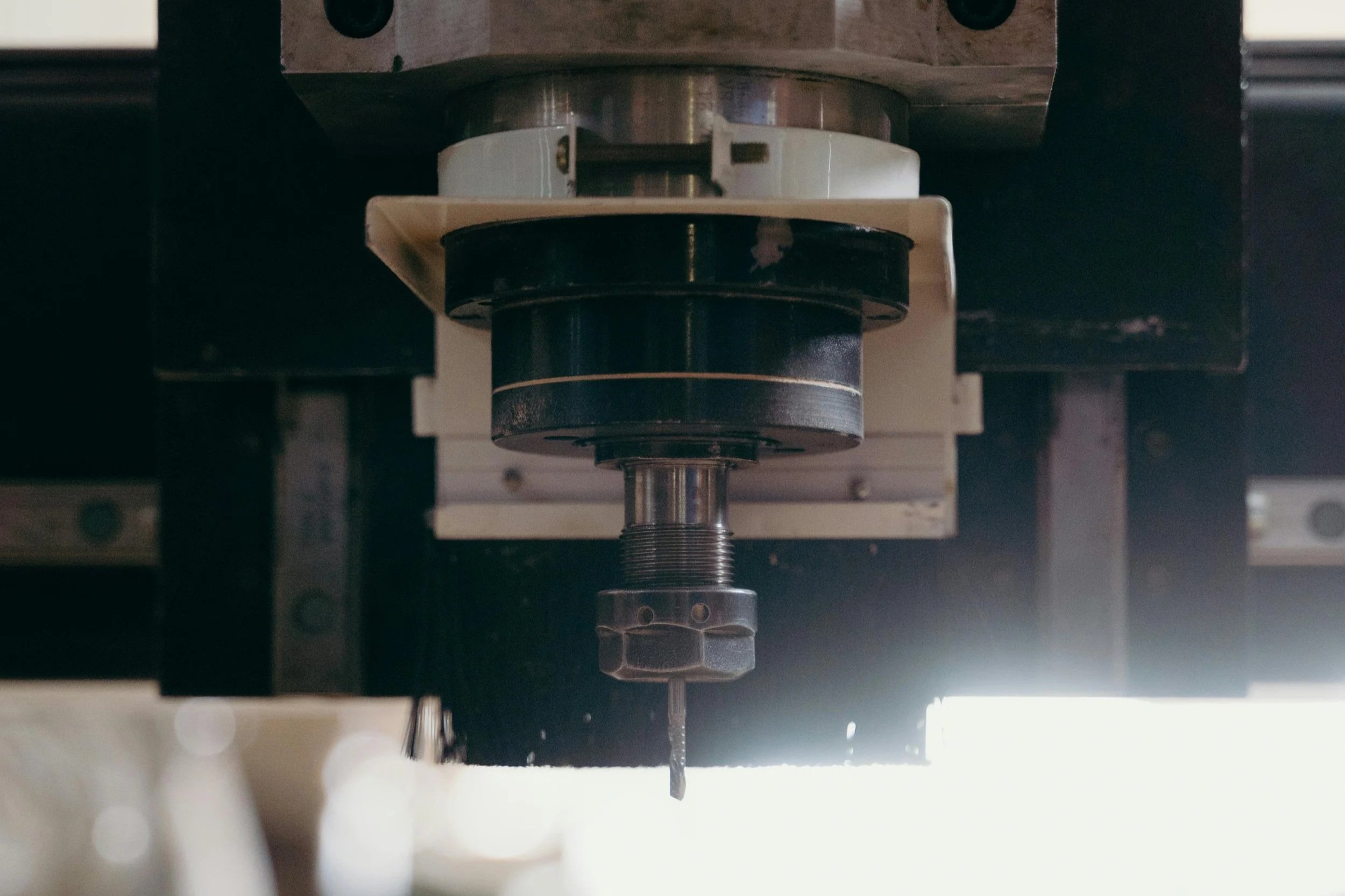 Vue en gros plan d'une partie de machine avec un axe central, un élément noir et blanc, et une mèche de perceuse suspendue en dessous.