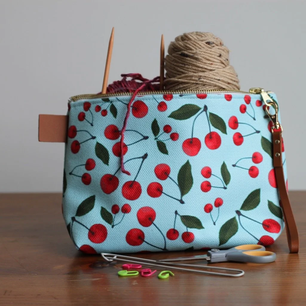 Image with Cherry Bounty Zippered Pouch filled with knitting supplies.  Blue background, red cherries and green leaves.
