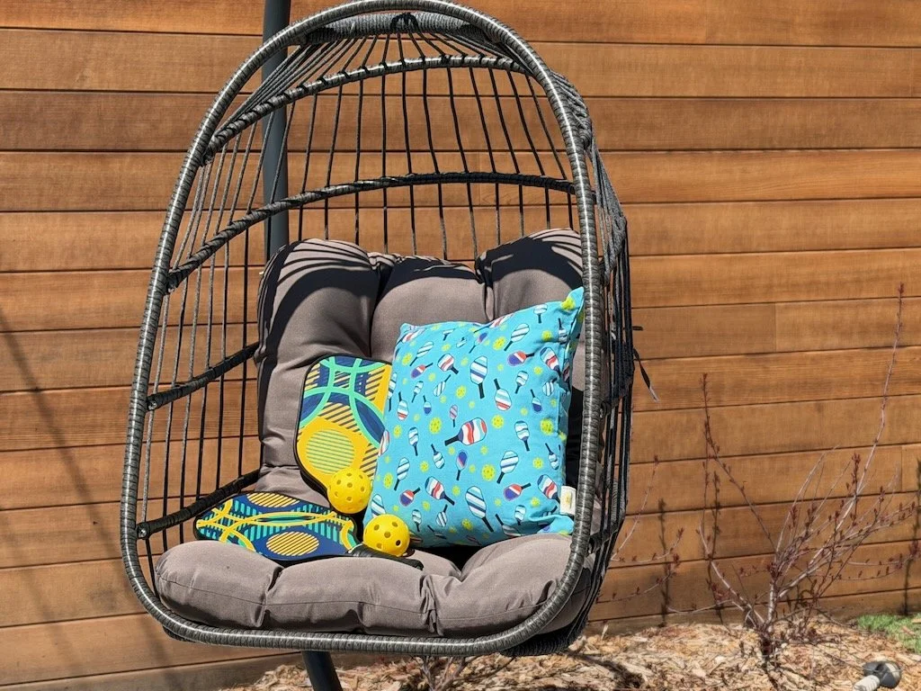 Image of swinging chair with blue pickleball pillow and pickleball raquets and balls