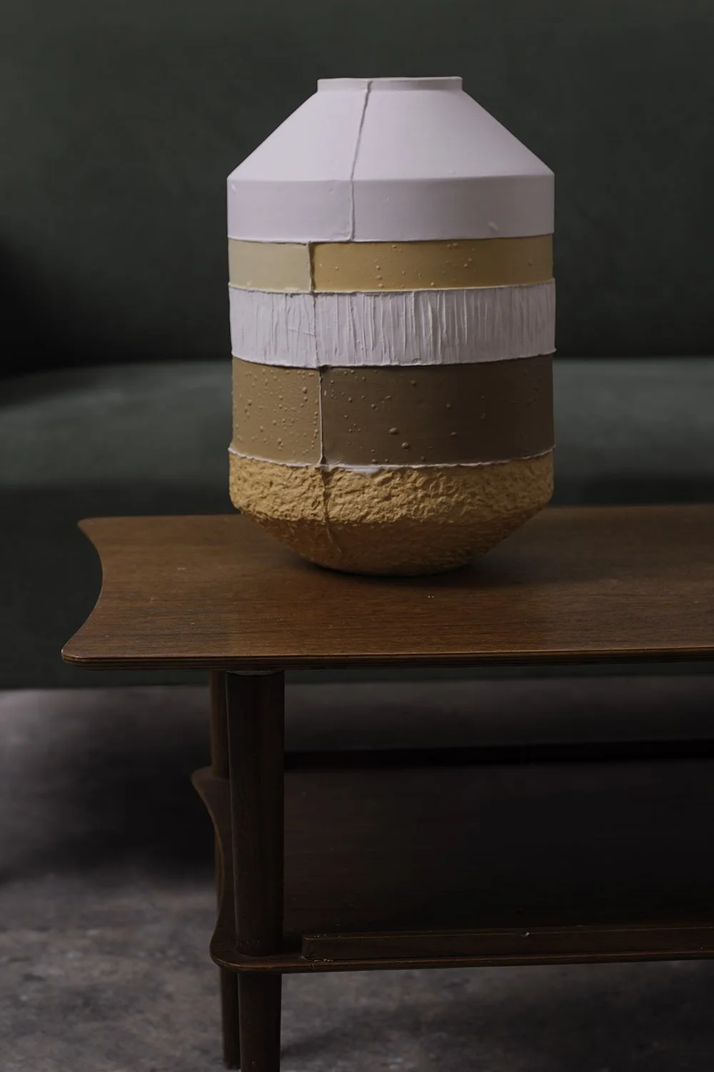 A decorative vase with horizontal bands of different textures and colors, placed on a wooden table against a dark background.
