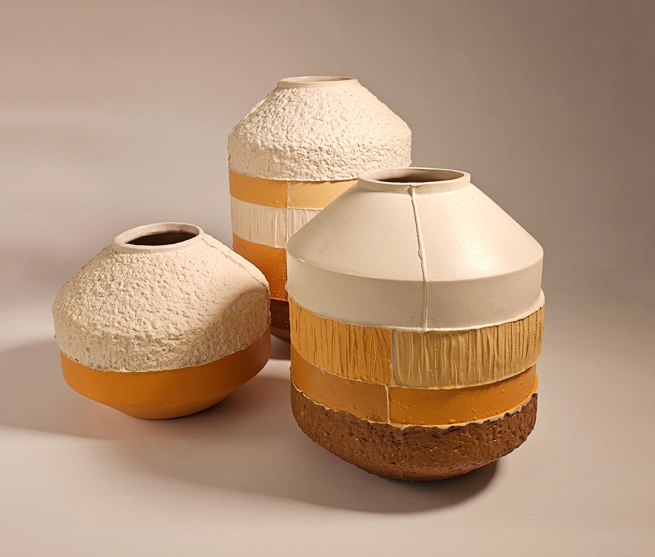 Three decorative ceramic vases with layered textures and colors, arranged on a white surface against a plain background.