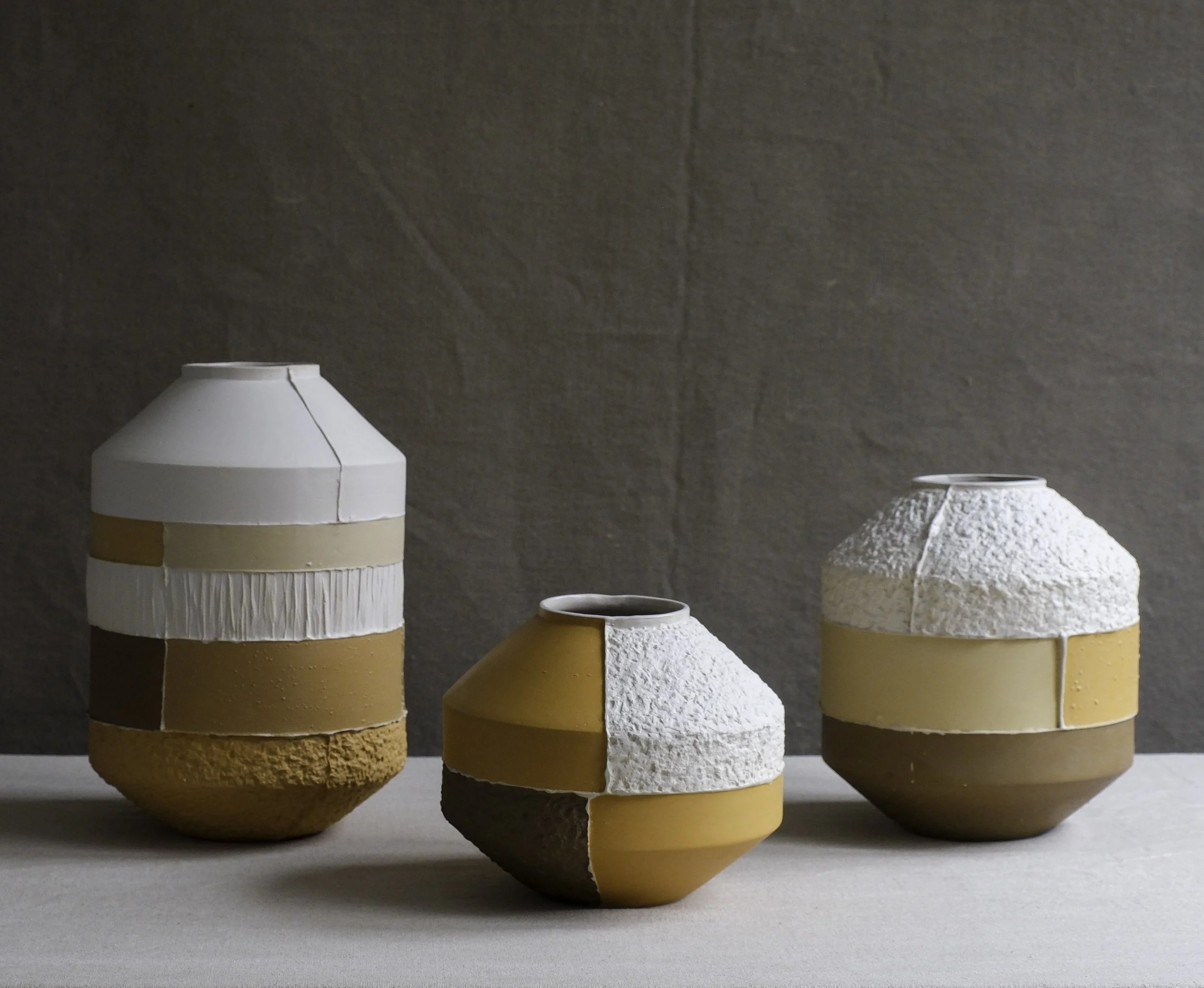 Three decorative ceramic planters on a white surface against a gray wall, each with textured and smooth surfaces in earthy tones.