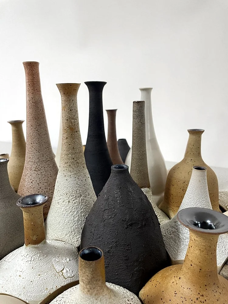 Close up of a collection of thrown bottle forms varying in height and colour that together form a ceramic landscape