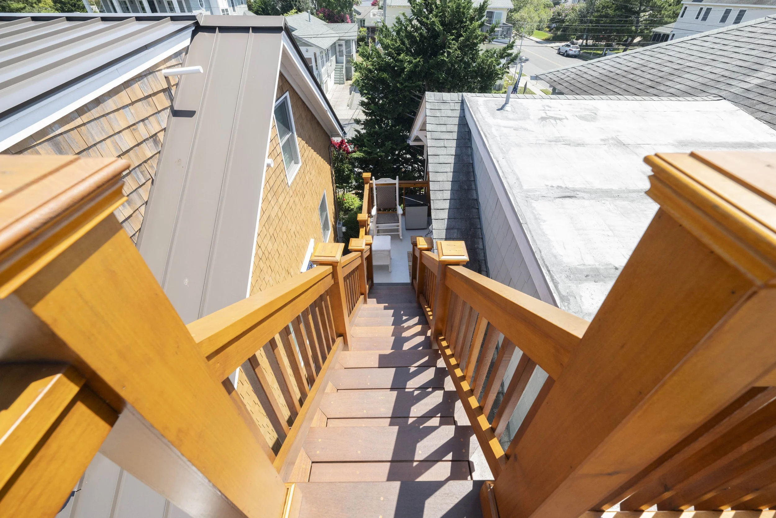 View from the top of a wooden staircase showing the backyard with patio furniture, a tree, and neighboring houses.