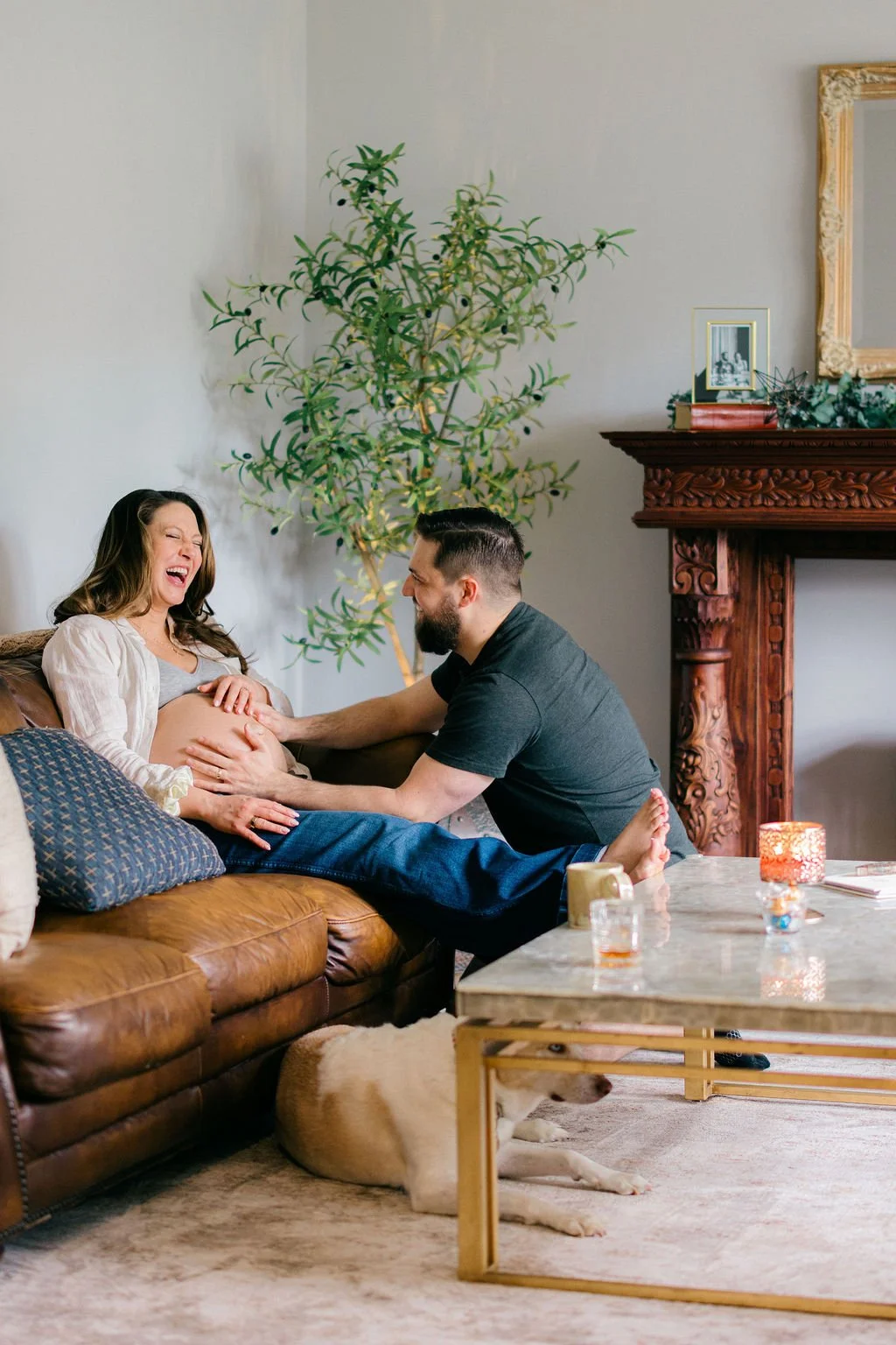 Expecting couple laughing together on a couch during an in-home maternity session in Sterling, Virginia.