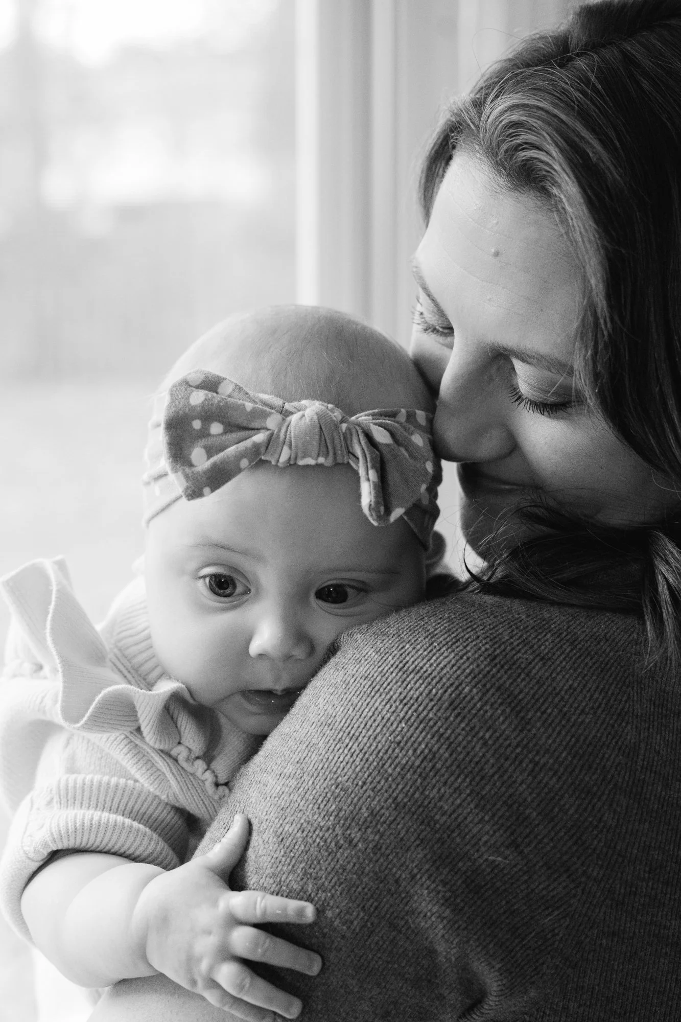  Mother holds her baby close by a window during an in-home family session in Sterling, Virginia 