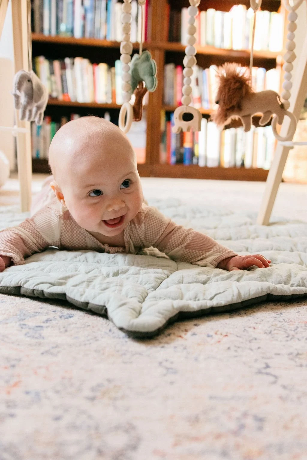  Baby smiling during tummy time on a quilted play mat under a wooden play gym at home in Sterling, Virginia. 