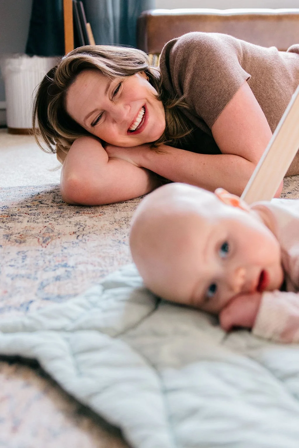  Mother lying on the floor smiling and laughing while watching her baby during tummy time on a play mat in Sterling, Virginia. 