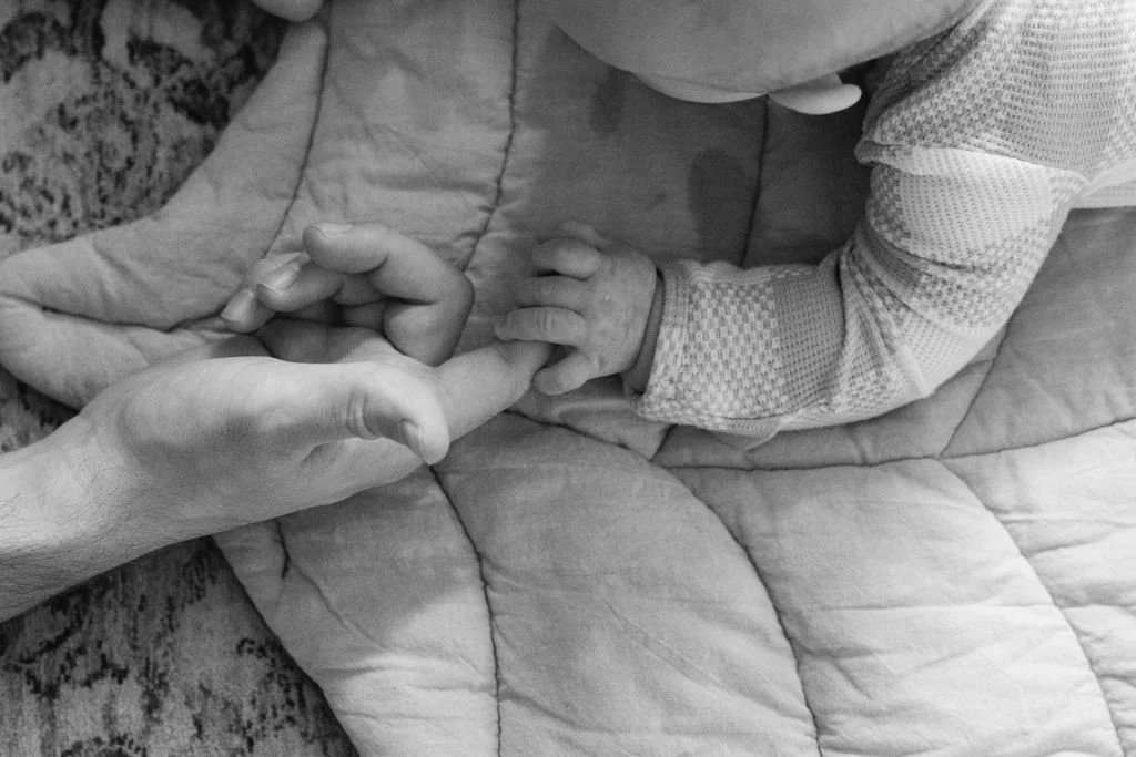  Close-up of a newborn baby holding a parent’s finger while lying on a play mat at home in Sterling, Virginia. 