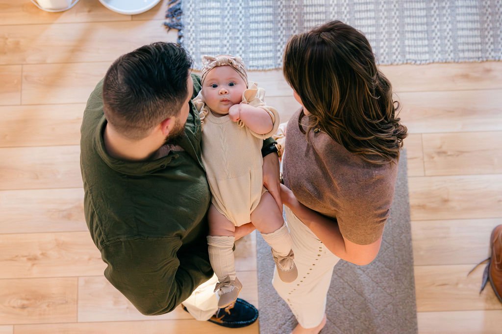  Overhead view of parents holding their baby together in the entryway of their home during a documentary family session in Sterling, Virginia. 