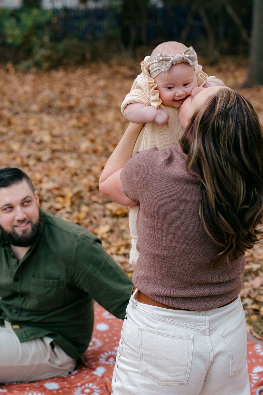  Mother kissing her baby while holding her outdoors in the backyard during a documentary family session in Sterling, Virginia. 