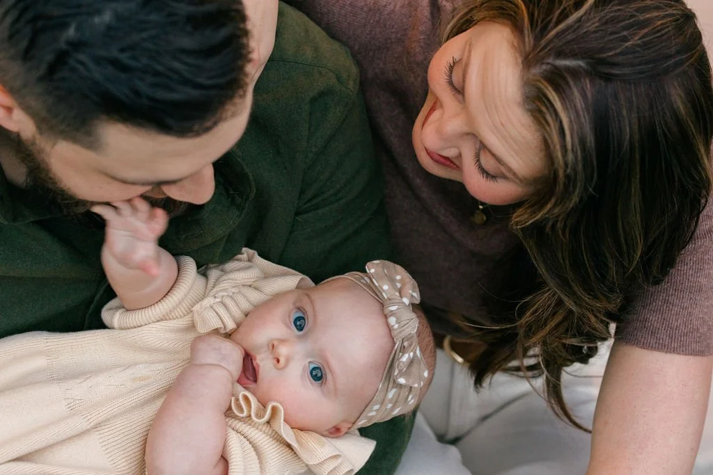  Father holding their baby, with the baby looking toward the camera and parents focused on her during a documentary family session in Sterling, Virginia. 