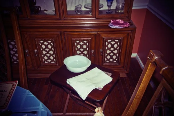 A hand washing station set up beside a wooden hutch for the Passover seder ritual, with a bowl and folded towel, captured as a documentary detail by Mel Usry Photography Northern Virginia.