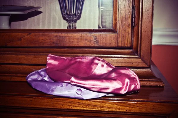 Two satin kippot in pink and purple resting on a wooden sideboard before the Passover seder begins, captured as a documentary detail by Mel Usry Photography Northern Virginia.