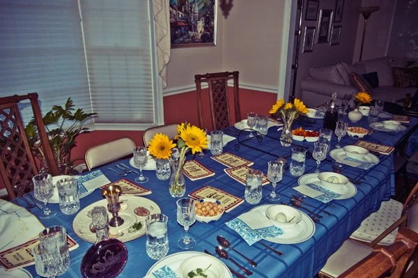 A Passover seder table set with sunflowers, crystal glasses, haggadahs, and blue patterned place settings, documented during a multi-generational family gathering by Mel Usry Photography Virginia.