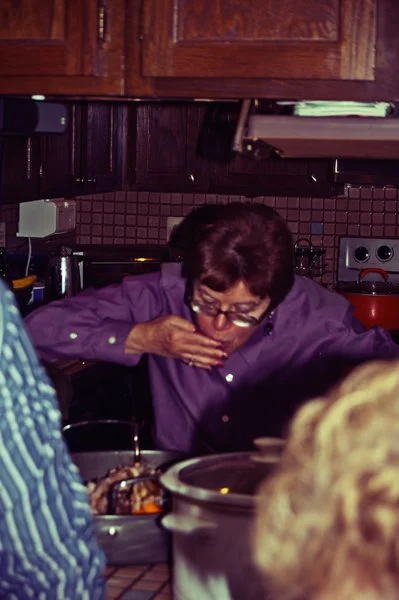 A woman in a purple shirt tastes food while working in the kitchen during Passover meal preparation, captured candidly behind the scenes by Mel Usry Photography Northern Virginia.