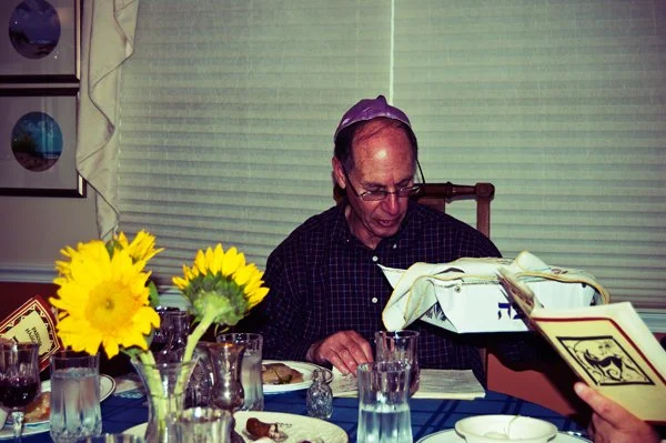 An older man wearing a kippah reads from a Passover haggadah at the seder table, captured candidly by documentary family photographer Mel Usry Photography in Northern Virginia.