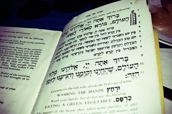 A close-up of an open Passover haggadah showing Hebrew text and English transliteration including the hand washing ritual, captured as a documentary detail by Mel Usry Photography Northern Virginia.