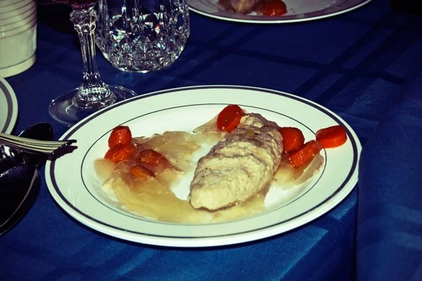 A plate of gefilte fish with carrots and broth on a blue tablecloth at a Passover seder dinner, documented as part of a multi-generational family gathering by Mel Usry Photography Northern Virginia.