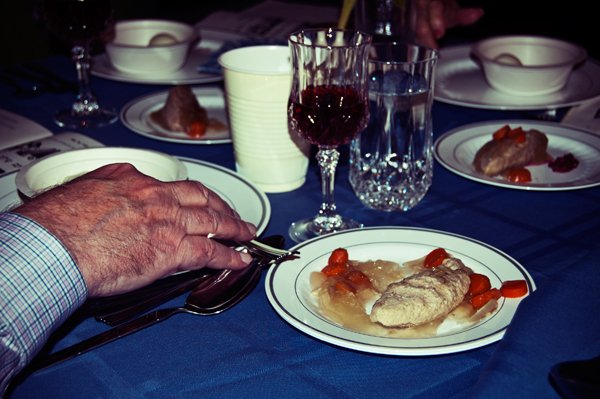 A man's hand holds silverware beside a plate of gefilte fish with carrots at the Passover seder table, documented candidly by Mel Usry Photography Northern Virginia.