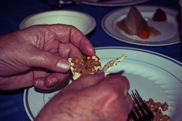 Close-up of hands holding a piece of matza topped with charoset at a Passover seder, a candid food detail captured by documentary family photographer Mel Usry Photography Northern Virginia.
