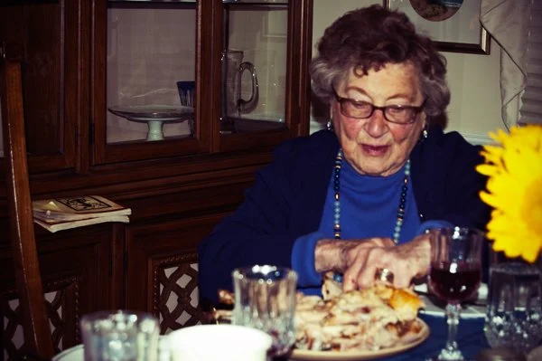 An older woman cuts food on her plate at the Passover dinner table, captured candidly during a multi-generational family gathering by Mel Usry Photography Northern Virginia.