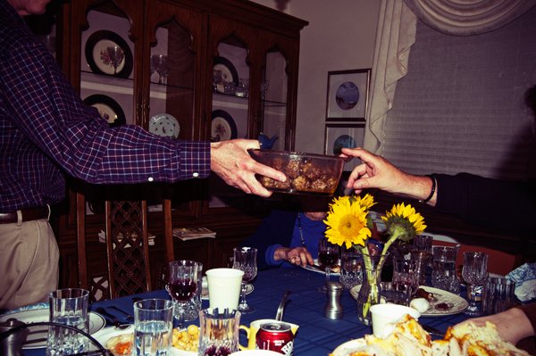 Two people pass a bowl of food across the Passover seder table past sunflower centerpieces, a candid connection captured by documentary family photographer Mel Usry Photography Northern Virginia.