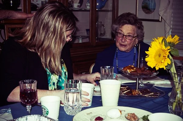 A young woman leans toward an older woman at the Passover seder table in a candid moment of connection, documented by documentary family photographer Mel Usry Photography Northern Virginia.