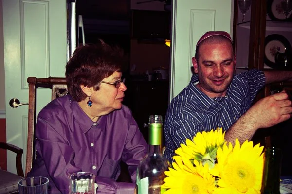 Two family members sit together at the Passover seder table with sunflowers and wine glasses in the foreground, captured candidly by Mel Usry Photography Northern Virginia.