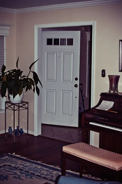 A quiet home entryway with a piano, potted plant, and front door captured as a documentary detail of the family home by Mel Usry Photography Northern Virginia.