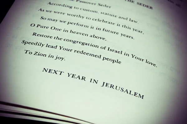 A close-up of the Passover haggadah open to the closing page reading "Next Year in Jerusalem," documented as a meaningful seder detail by Mel Usry Photography Northern Virginia.