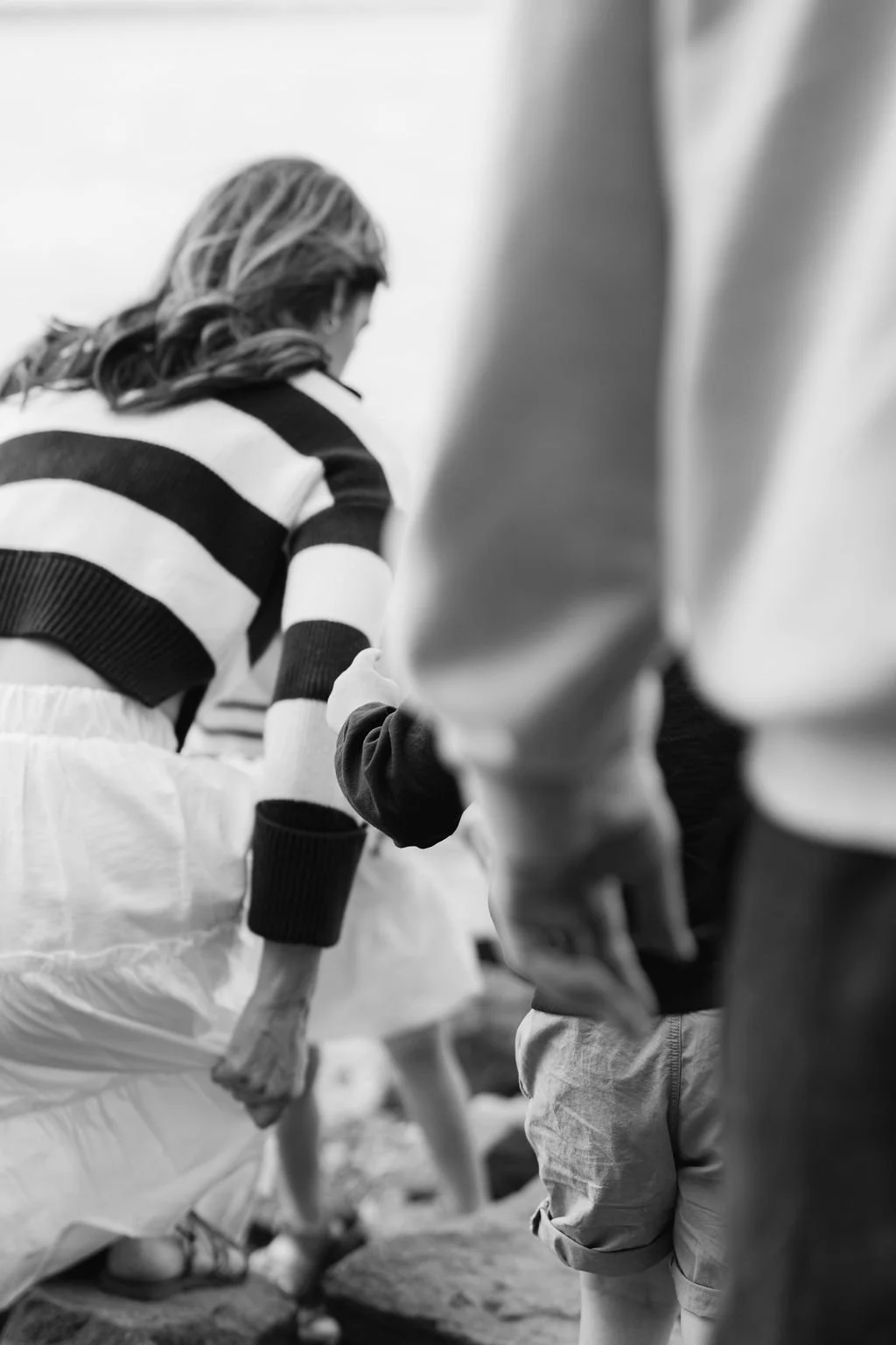A documentary photograph showing a family moving together outdoors, with layered movement and partial figures visible during a family session at Jones Point Park in Alexandria, Virginia.