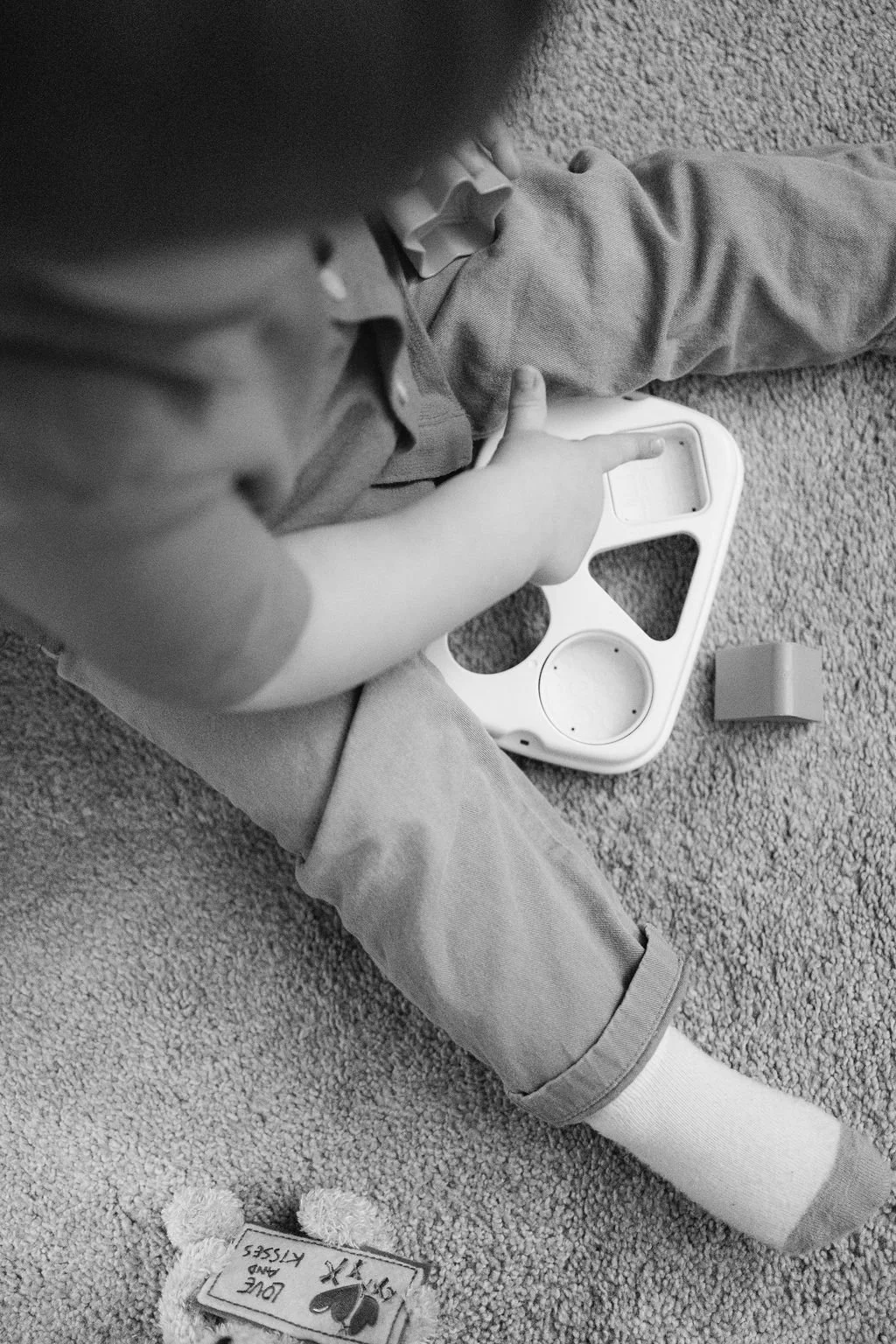 A black and white documentary family photograph of a toddler sitting on the floor playing with a toy during an in-home family session in Sterling, Virginia.