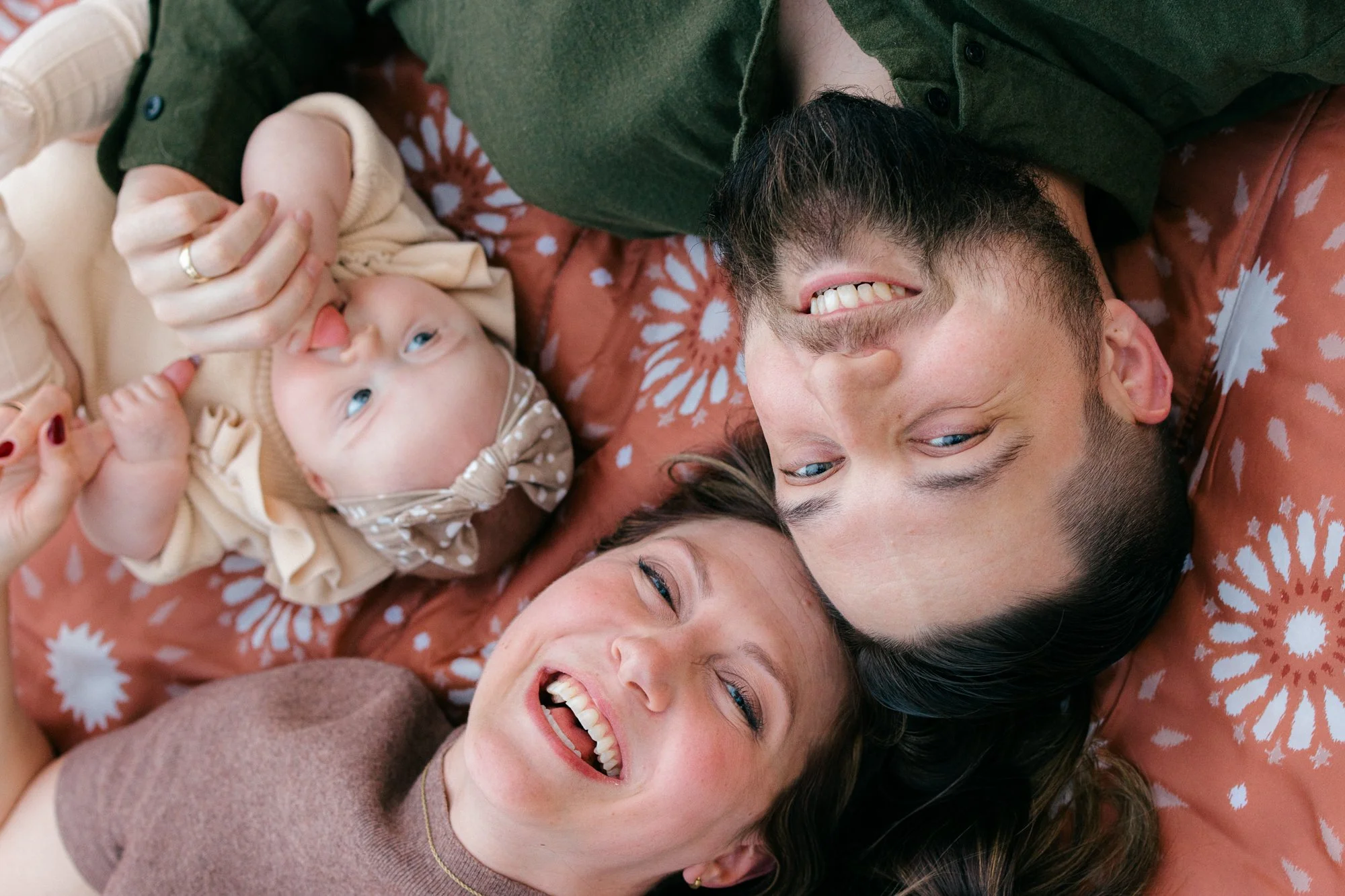 Parents and their baby lying together and laughing during an in-home documentary family session in Sterling, Virginia